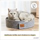 Eine graue Katze, die in einem runden, filzartigen Haustierbett mit einem Lederetikett liegt, mit dem Text 'Optimale Größe zum Kratzen & Liegen.'