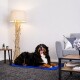 Ein glücklicher Berner Sennenhund liegt auf einer blauen Matte in einem gemütlichen Wohnzimmer, neben einer stilvollen Lampe und einem grauen Sofa.