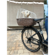 Ein kleiner Hund schaut aus einem Korb für Fahrräder mit einem weißen Sicherheitskäfig, der an einem schwarzen Fahrrad auf einem gepflasterten Untergrund befestigt ist.