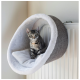 Eine graue getigerte Katze sitzt bequem in einem runden, plüschigen Katzenbett, das auf einem Heizkörper montiert ist, mit einem weichen weißen Innenraum.