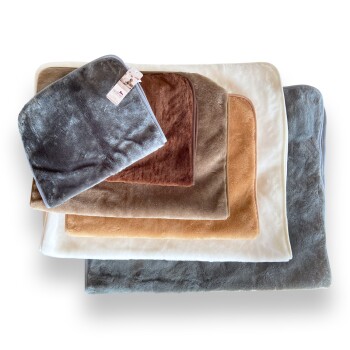 Ein Stapel von fünf weichen Tierdecken in verschiedenen Farben: grau, braun, beige und creme, mit einem kleinen Etikett, das an der obersten Decke befestigt ist.