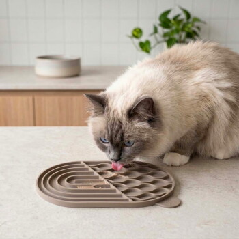 Eine flauschige, hellfarbige Katze leckt eine graue Silikon-Futtermatte mit einer strukturierten Oberfläche, die für Haustiermahlzeiten konzipiert ist.