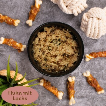 Schüssel mit zerkleinertem Huhn und Lachs, umgeben von Hundeleckerlis und einer Pflanze, mit dem Text "Huhn mit Lachs" am unteren Rand.