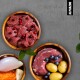 Drei Holzschalen gefüllt mit rohem Fleisch, Cranberries, Kartoffeln, Heidelbeeren und geriebenen Karotten, vor einem grauen Hintergrund.