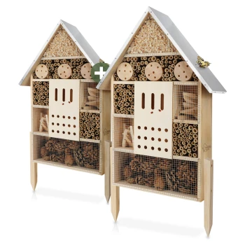 Zwei hölzerne Insektenhotels in Form von Häusern, die verschiedene Fächer mit natürlichen Materialien für nützliche Insekten enthalten.