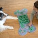 Ein Hund und eine Person interagieren mit einer grünen und grauen, knochenförmigen Puzzlematte mit Texturen und Verstecken für Leckerlis.