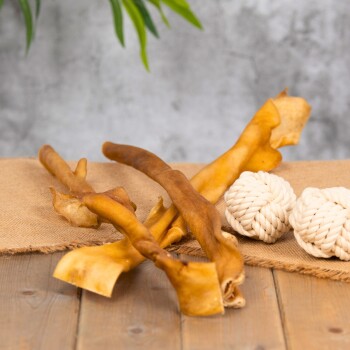 Eine Auswahl an Hundekauartikeln aus natürlichen Zutaten, einschließlich gedrehter Rohledersticks und zwei weißen Seilspielzeugen, auf einer Juteschicht.