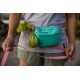 Eine Person hält eine rosa Leine in einer Hand und eine grüne Tasche, die an einem türkisfarbenen Ruffwear-Hüftgurt befestigt ist, in der anderen Hand, im Freien.