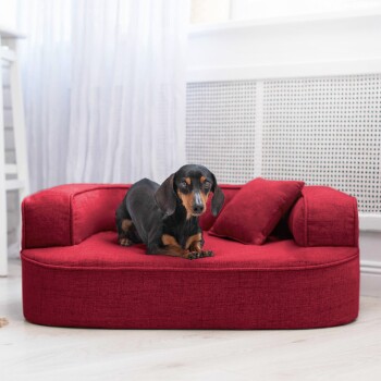 Rotes Haustiersofa mit gepolstertem Boden und zwei seitlichen Kissen, mit einem kleinen passenden Kissen, auf einem hellen Holzboden.
