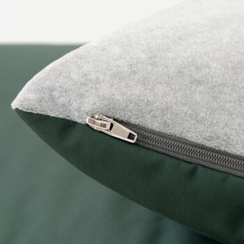 Nahaufnahme einer Ecke eines Haustierbettes mit einem grauen Fleece-Oberteil und einem grünen Stoffboden, mit einem sichtbaren Reißverschluss für einfache Entfernung.