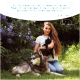 Eine Frau im Freien mit Blumen hält eine schwarze Katze, während ein wolfähnlicher Hund neben ihr liegt. Text oben bewirbt Wolfsbacher Natur Produkte.