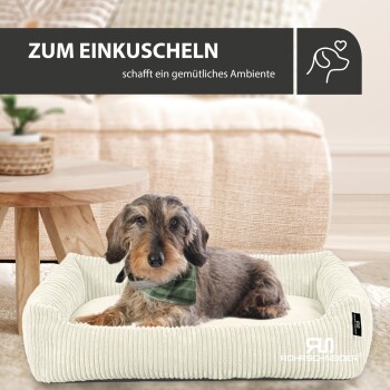Ein Dackel in einem grünen Halstuch ruht auf einem gemütlichen Hundebett, mit einem Holztisch und weichen Möbeln in der Nähe. Text: 'ZUM EINKUSCHELN.'