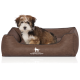 Flauschiger braun-weißer Welpe sitzt in einem braunen rechteckigen Hundebett mit 'KNUFFELWUFF'-Logo und Hundesilhouette auf der Vorderseite