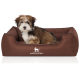 Ein kleiner, flauschiger Hund sitzt bequem in einem braunen Hundebett mit dem Logo "KNUFFELWUFF" auf der Vorderseite.