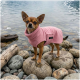 Ein brauner und schwarzer Hund, der ein weiches rosa Handtuch trägt, von hinten gesehen, vor einem schlichten weißen Hintergrund.