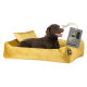 Ein glücklicher brauner Labrador-Retriever ruht auf einem plüschigen gelben Hundebett mit einem kleinen Kissen, das ein Etikett mit der Aufschrift "+ Kotbeutel Set" trägt.