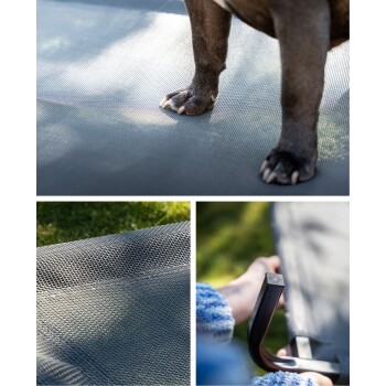 Eine Nahaufnahme einer Hundepfote auf einer strukturierten grauen Haustiermatte, mit einer Hand, die die Kante der Matte im Hintergrund hält, auf grünem Gras.