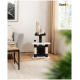 Eine hellgraue Katze sitzt auf einem schwarz-weißen Kratzbaum in einem gemütlichen Wohnzimmer, mit einem Couchtisch und einem Fenster im Hintergrund.