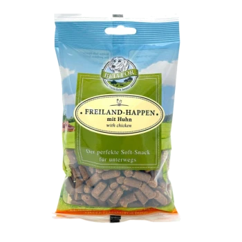 Eine durchsichtige Tüte mit Hundeleckerlis, beschriftet mit "FREILAND-HAPPEN mit Huhn" mit malerischem Hintergrund und "Der perfekte Soft-Snack für unterwegs."