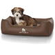 Flauschiger braun-weißer Welpe sitzt in einem braunen Hundebett mit der Aufschrift 'KNUFFELWUFF' und weißem Hundelogo.