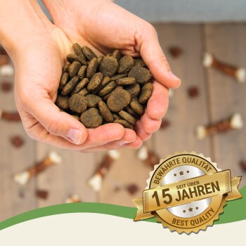 Hände halten einen Haufen dunkler, runder Haustierfutterkibble, mit einem Abzeichen, das "Bewährte Qualität seit über 15 Jahren" und "Beste Qualität" angibt.