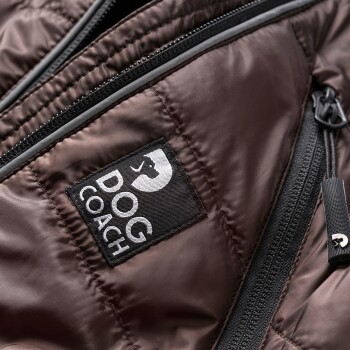Nahaufnahme einer braunen Haustierjacke mit dem 'DOG COACH'-Logo auf einem schwarzen Patch, mit sichtbaren Reißverschlüssen und Stofftextur.