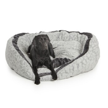 Ein schwarzer Labrador Retriever, der bequem in einem plüschigen, grauen Haustierbett mit einer weichen, strukturierten Oberfläche und einem gemütlichen Design liegt.