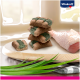 Ein Stapel grüner und brauner Haustierleckereien auf einem Holzschneidebrett, mit einem rohen Hühnerbein im Hintergrund. Vitakraft-Logo sichtbar.
