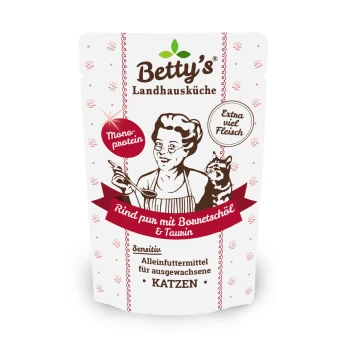 Betty's Landhausküche Katzenfutter zeigt eine Frau, die mit einer Katze kocht, beschriftet mit "Rind pur mit Bonretschöl & Taurin," und betont "Extra viel Fleisch."