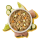 Schüssel mit stückigem Nassfutter für Haustiere mit gewürfeltem Gemüse, umgeben von rohen Hühnerstücken, Salat und Zucchinischeiben auf gelbem Hintergrund.