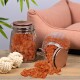 Zwei Glasbehälter mit orange-braunen Haustierleckereien, einer umgekippt auf einer Holzoberfläche, mit einem rosa Haustierbett und Seilspielzeugen im Hintergrund.