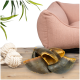 Ein gemütliches pinkes Haustierbett steht im Hintergrund neben einer Holzoberfläche mit einem Haufen großer, zerbrochener Muscheln und einem weißen Seilspielzeug.
