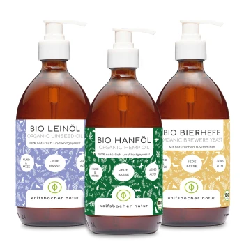 Drei Flaschen organischer Haustierergänzungen: Leinsamenöl, Hanföl und Brauereihefe, jede mit bunten Etiketten und Pumpenspendern.