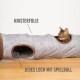 Eine verspielte Bengal-Katze schaut aus einem grauen Haustiertunnel mit braunem Rand heraus, mit Textetiketten "KNISTERFOLIE" und "JEDES LOCH MIT SPIELBALL."