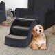 Eine schwarze Haustiertreppe mit drei Stufen, mit einer weichen, beigen Teppichoberfläche, neben einem Stuhl in einem gemütlichen Wohnzimmer platziert.