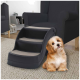 Eine schwarze Haustiertreppe mit drei Stufen, mit einer weichen, beigen Teppichoberfläche, neben einem Stuhl in einem gemütlichen Wohnzimmer platziert.
