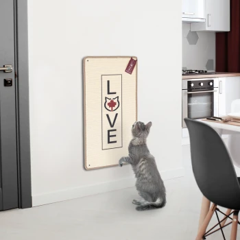 Eine graue Katze steht auf ihren Hinterbeinen und schaut neugierig auf ein wandmontiertes Kratzbrett mit "LIEBE" und einer Katzensilhouette.