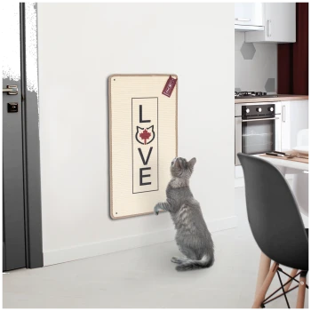 Eine graue Katze steht auf ihren Hinterbeinen und schaut neugierig auf ein wandmontiertes Kratzbrett mit "LIEBE" und einer Katzensilhouette.