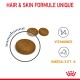 Croquettes pour animaux de compagnie brunes affichées avec un accent sur un morceau, étiquetées "HAIR & SKIN FORMULE UNIQUE," avec des icônes pour les vitamines et les Oméga-3 & 6.
