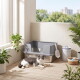 Grau-weiße Katze liegt auf einer Matte neben einer grauen, abgedeckten Katzentoilette mit Schaufel, einem Vorratsbehälter und einem Korb mit Spielzeug auf einem sonnenbeschienenen Balkon.