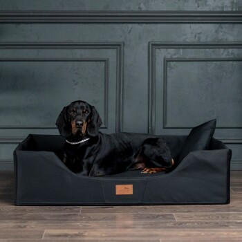 Ein graues Haustierbett mit abnehmbarem Bezug, mit einem Lederetikett, auf einem Holzboden gezeigt.