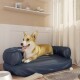 Ein entspannter Corgi, der auf einem blauen Haustierbett in einem gemütlichen Raum mit hellen Vorhängen, einer Hundeschale und einem Kauspielzeug in der Nähe liegt.