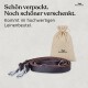 Leder-Hundeleine mit Metallverschlüssen und einem beigen Leinensäckchen mit Kordelzug, Text auf Deutsch über Geschenkverpackung.