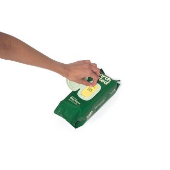 Eine Hand greift nach einem Packung Earth Rated Hundetüchern, mit einer grünen Verpackung und einem gelben Klappdeckel, auf dem steht: "Hundetücher."