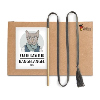 Ein Kartonpaket mit einer Cartoon-Katze in Brille und Schal, beschriftet mit "KATER KASIMIR RANGELANGEL GRAU," mit einem Holzstock und grauem Quastenschnur.