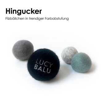 Vier Wollfilzbälle (schwarz, grau, hellgrau, mint); schwarzer Ball mit Stickerei 'LUCY BALU'; Überschrift 'Hingucker'.