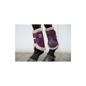 Eine Nahaufnahme der Beine eines Pferdes, das lila Schutzstiefel mit weichem Futter trägt, wobei das Markenlogo an den Riemen zu sehen ist.