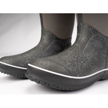Graue Gummistiefel mit Blumenmuster und weißem Rand, die eine strukturierte Sohle für besseren Halt zeigen.