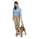 Eine Frau in einem hellblauen Hemd und beigen Hosen steht und hält eine Leine, die an einem glücklichen, braunen Bulldoggen befestigt ist.