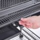 Eine Hand zieht an einem Metallgriff eines Drahtkäfigs für Haustiere, der ein geräumiges Inneres mit einem abnehmbaren Tablett darunter zeigt.